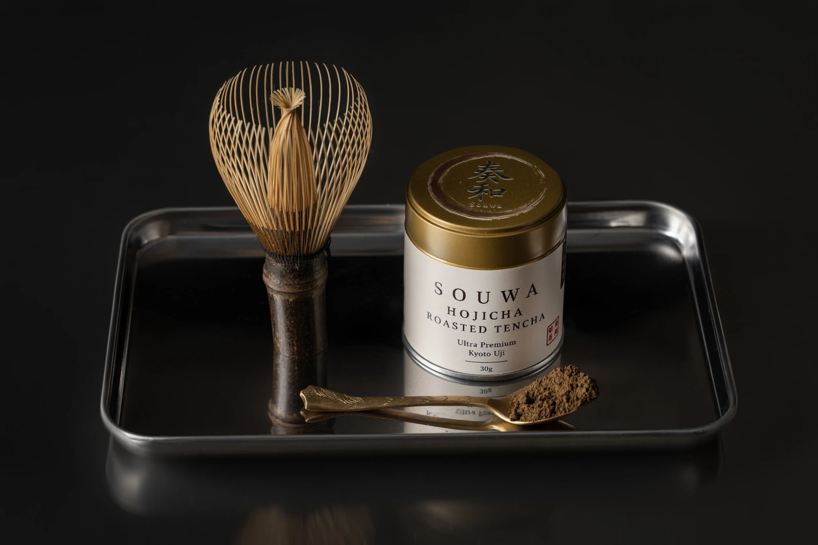 กระป๋อง SOUWA Hojicha คู่กับฉะเซ็นและผงชาคั่วบนถาดสีเข้ม